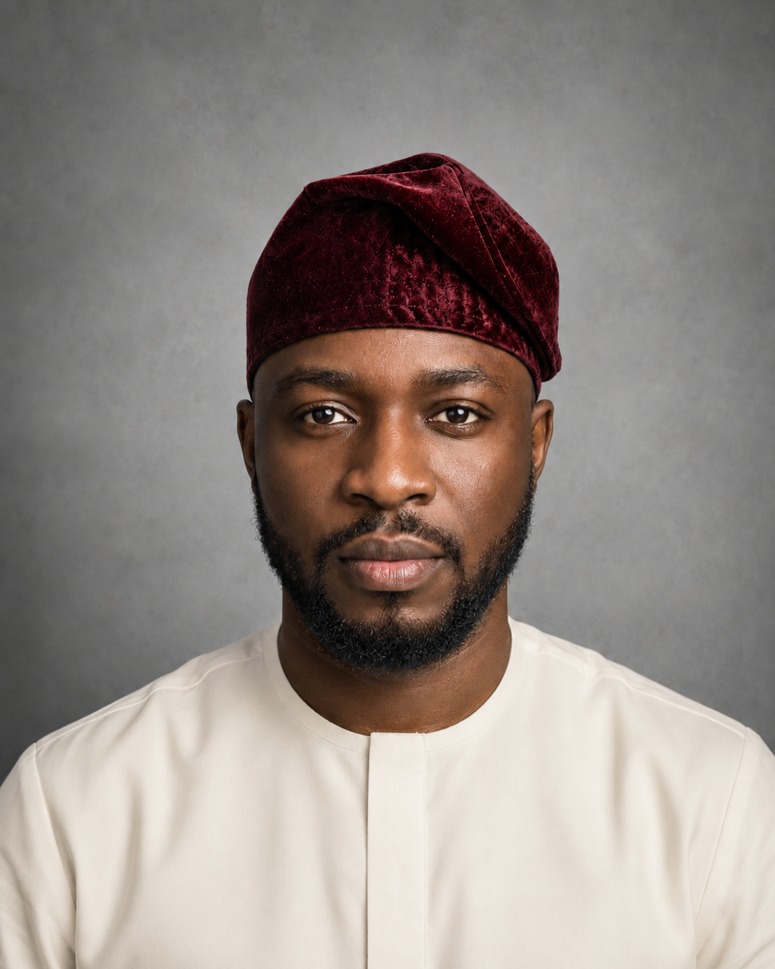 Male model wearing an Orí Adé burgundy velvet Yoruba fila cap with an ivory kaftan.