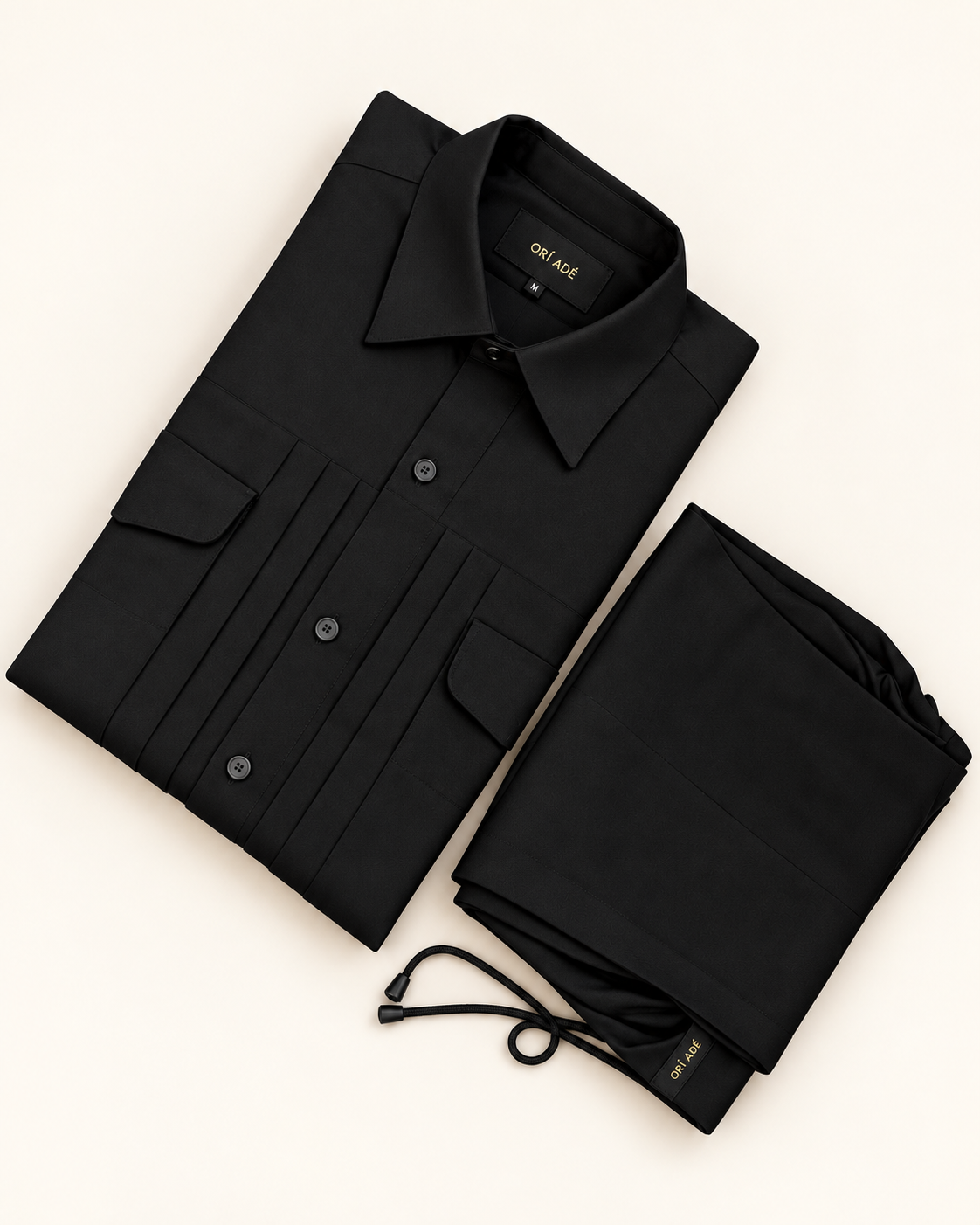 Orí Adé black pleated pocket shirt with matching drawstring trousers, folded on an off-white background